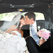 A bride and groom kissing in the back of their limo.